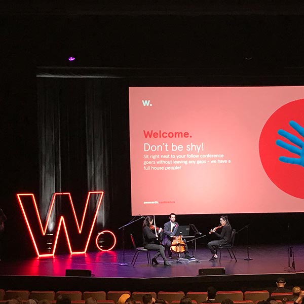 3 musicians sit on stage playing music for the opening of the conference.