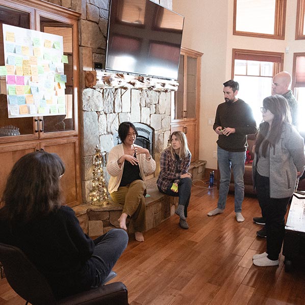 The team stands in a circle discussing post-it notes on the wall.