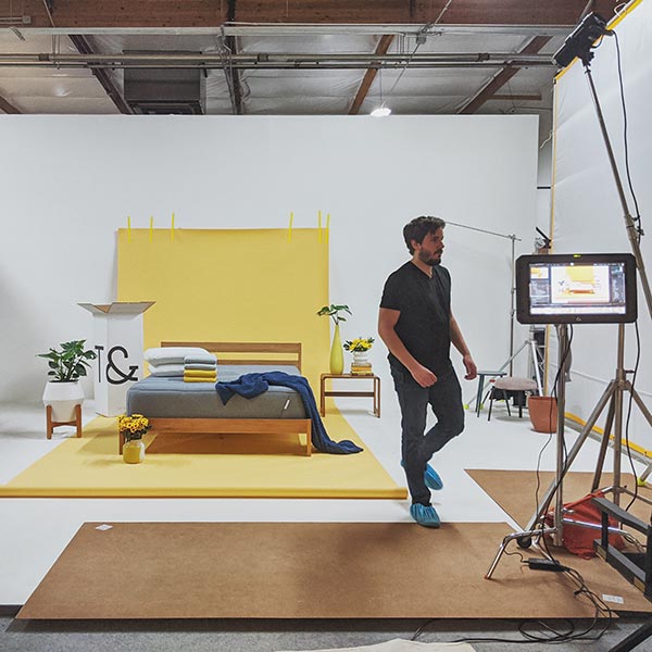 A mattress and bed frame sits on a cyclorama on top of yellow seamless paper.