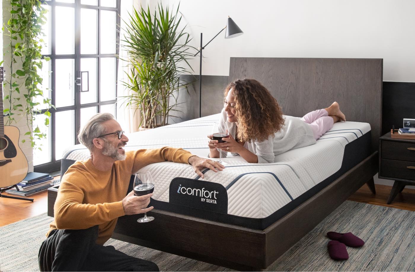 A man and woman drinking wine on an iComfort mattress in a bedroom