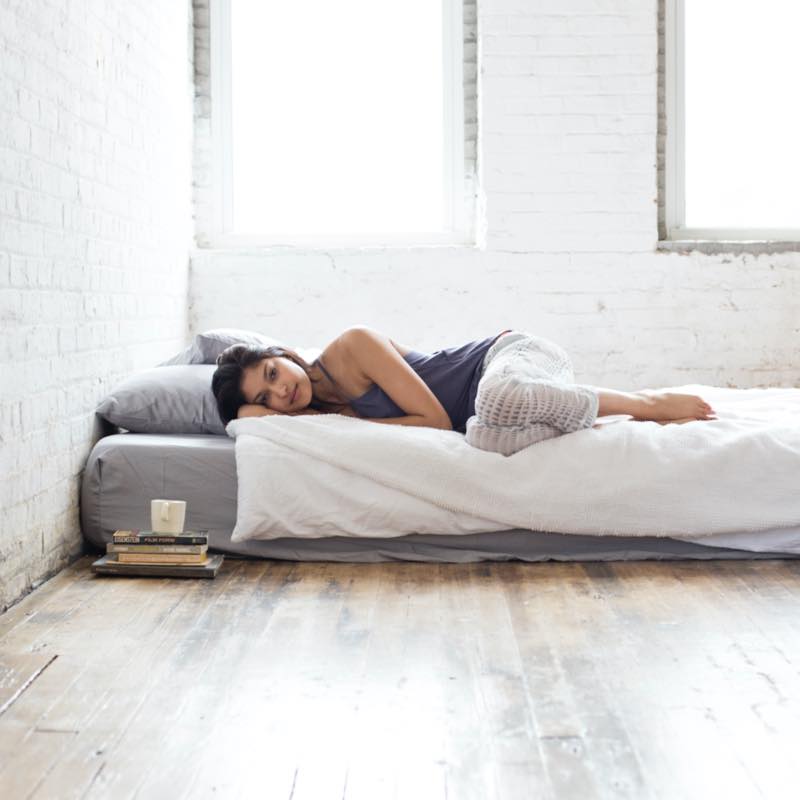 On old-style lifestyle image of a woman on bed in a stark loft space. The mattress sits on the floor.