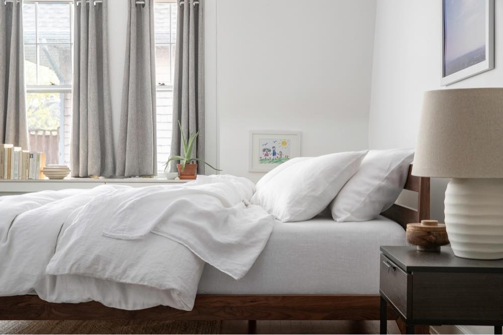 A side shot of a cozy made bed with white linen sheets and duvet cover.